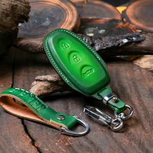 May include: Green leather key fob with a silver key ring and a matching green leather strap. The fob has three buttons and a car icon embossed on the front.