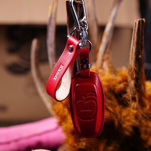 May include: Red leather keychain with a silver clasp. The keychain features a red leather strap with the name "Kandi" and a red case with an apple design and the name "Kandi".