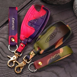 Puede incluir: Tres llaveros con patrones de camuflaje y nombres personalizados. Los llaveros están hechos de cuero y tienen un anillo de metal. Los nombres en los llaveros son "Christy", "Jeffrey" y "Jesús".