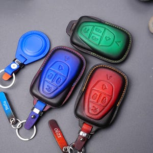 May include: Four key fobs with leather covers in different colours: green, blue, red, and blue. The key fobs have four buttons each and are attached to keychains.