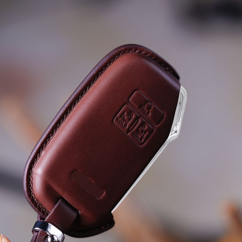 May include: A brown leather key fob with a silver trim. The fob has three buttons labeled "Hold", "Lock", and "Unlock".