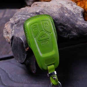 May include: A green leather key fob with four buttons, including a "Panic" button. The fob has a silver ring and a green leather strap.