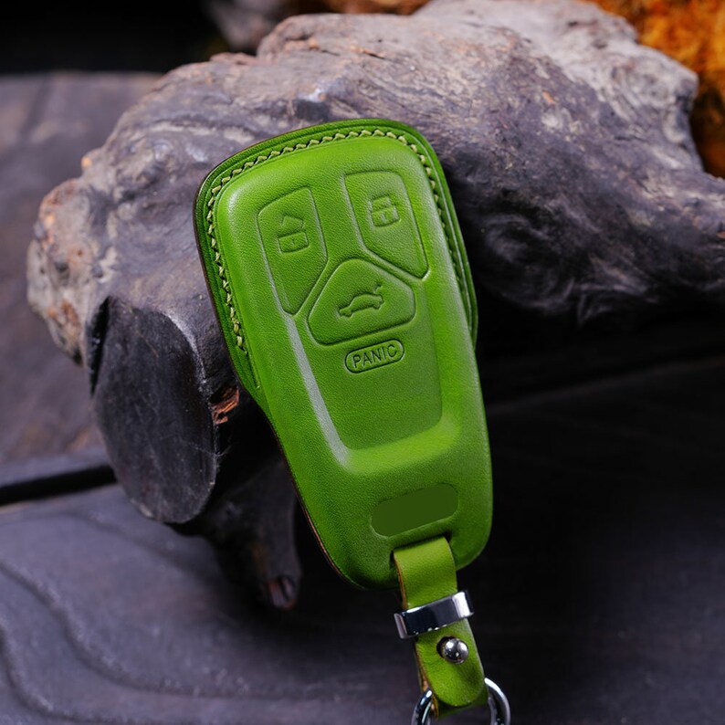 May include: A green leather key fob with four buttons, including a "Panic" button. The fob has a silver ring and a green leather strap.