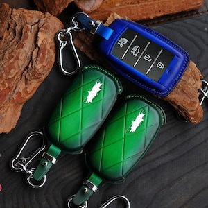 May include: Two green leather key covers with a diamond pattern and a white logo. A blue leather key cover with a silver key fob and buttons.