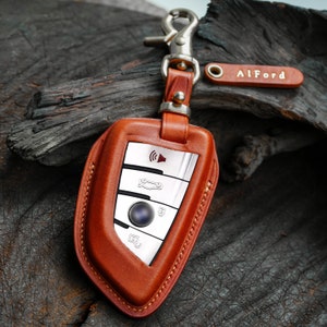 Peut inclure: Un porte-clés en cuir marron avec une télécommande d'entrée sans clé argentée à l'intérieur. Le porte-clés a un crochet en métal argenté et une petite étiquette en cuir qui dit "AlFord".