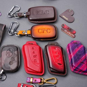 May include: Assortment of ten leather keychains with different designs and colours. Some keychains have personalised text, such as "KLC" and "CPC".