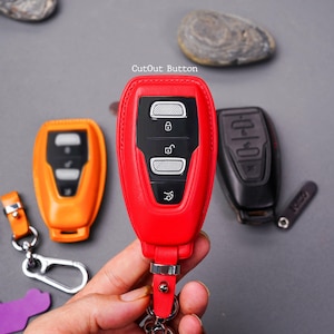 May include: Three different key fobs with leather covers. The key fobs are red, orange, and black. The red key fob has the text "CutOut Button" on it. The key fobs have multiple buttons.