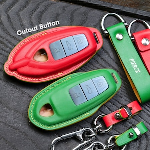 May include: Two leather key covers, one red and one green, with a cutout for a button. The covers are stitched with yellow thread. The covers are attached to leather keychains with metal rings. The keychains are green and red with the word "PIERCE" embossed on the green keychain.