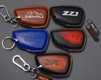 May include: Leather key fob covers in brown, black, and blue, featuring embossed logos and text like "DENALI", "ZZ1", and "ZR2". Each cover has a metal keyring and a carabiner clip for attachment.