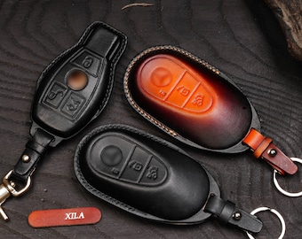 May include: Three leather key covers for car keys. The covers are black, brown, and orange. The covers have stitching around the edges and a key ring attached.