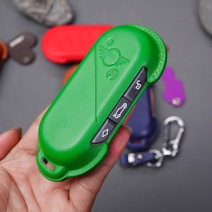 Può includere: Portachiavi in ​​pelle verde con un'icona di un'auto e un pulsante con la scritta "5".