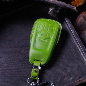 May include: A green leather key fob with four buttons, including a panic button. The fob has a silver metal key ring attached.