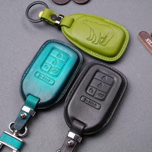 May include: Three leather keychains with key fobs. One keychain is green with a polar bear design. One keychain is teal with a key fob that has a silver "3D Gold" inscription. One keychain is black with a key fob that has a silver "3D Gold" inscription.