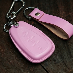 May include: Pink leather key fob with a silver key ring and a pink leather strap. The key fob has three buttons with raised symbols.