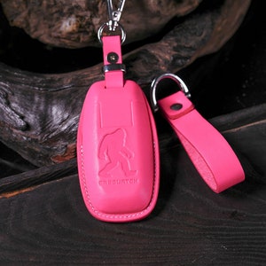 May include: Pink leather key fob with a stitched edge and a silver metal loop. The fob has a raised image of a Bigfoot and the text "Sasquatch".