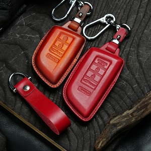 May include: Two leather key covers with key rings. One is red and the other is orange. Both have a silver metal key ring.
