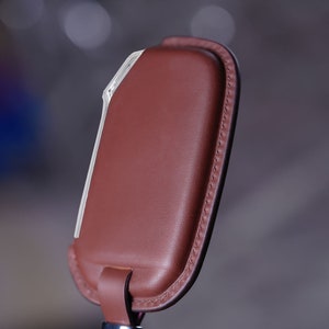 May include: A brown leather key holder with a white trim and a stitched edge.