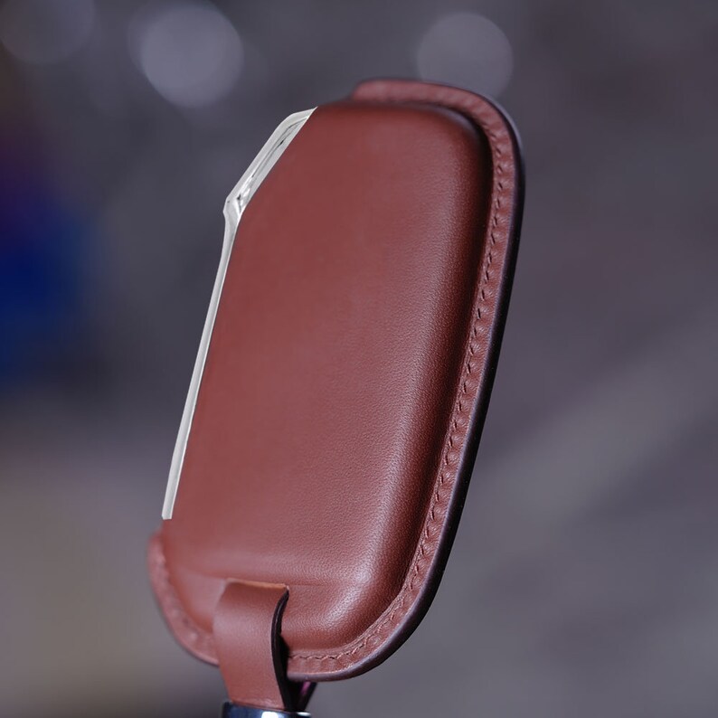 May include: A brown leather key holder with a white trim and a stitched edge.