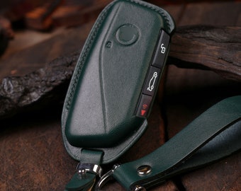 May include: A green leather key fob with a silver key ring and a matching green leather strap. The key fob has a button with a car icon and a button with a wireless signal icon.