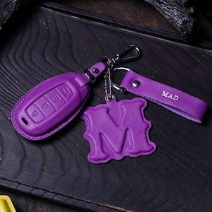 May include: Purple leather key fob with a silver key ring and a purple leather charm with the letter "M" and the word "MAD" embossed on it.