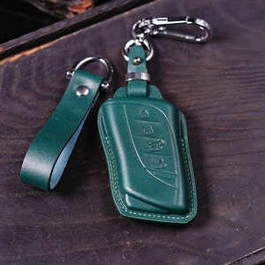 May include: A green leather key fob with a silver metal clasp and a green leather strap. The key fob has a stitched edge and a design of four buttons.
