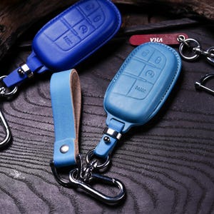 May include: A close-up shot of several leather key fob covers in shades of blue. The covers have button imprints and are attached to keychains with metal clasps. One cover has the word "PANIC" printed on it.