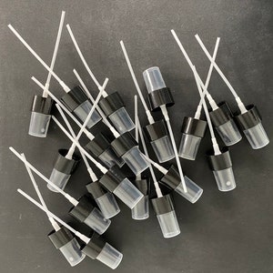 May include: A group of black and clear plastic spray bottle tops with white tubes attached. The tops are arranged in a pile on a dark gray surface.
