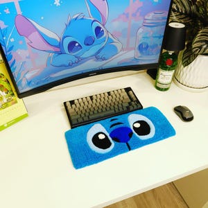Könnte beinhalten: Ein blauer Schreibtisch mit Tastatur, Maus und einer Handgelenkauflage im Stitch-Design. Die Handgelenkauflage hat einen blauen Hintergrund mit Stitchs Gesicht. Ein Computermonitor zeigt ein Stitch-Bild. Eine Flasche und eine Pflanze sind ebenfalls zu sehen.