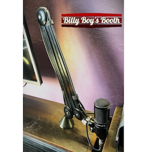May include: Black microphone arm with a black microphone attached to it. The arm is extended and the microphone is positioned in front of a computer monitor. The text "Billy Boy's Booth" is visible in the background.