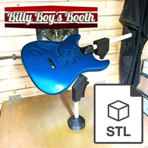 May include: A blue electric guitar body is mounted on a 3D printed stand. The stand is designed to hold the guitar body in place while it is being painted. The stand is made of black plastic and has a white base. The stand is labelled with the text "STL" indicating that the design is available as a 3D printable file.