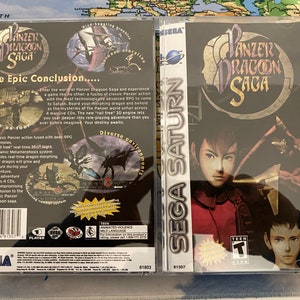 May include: A Sega Saturn video game case for Panzer Dragoon Saga. The front of the case features a character with red hair and a blue shirt. The back of the case has a description of the game and a rating of Teen.