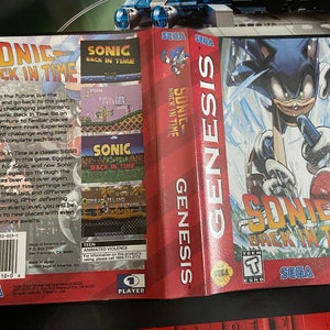 May include: A Sega Genesis game cartridge for Sonic Back in Time. The front of the box features a blue Sonic the Hedgehog running through a snowy landscape. The back of the box shows screenshots from the game and information about the game.