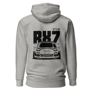 Pode incluir: Uma jaqueta de moletom cinza com um gráfico preto de um carro Mazda RX7 com o texto "Mazda RX7" em japonês nas costas.