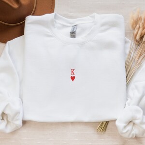 May include: White sweatshirt with a red embroidered heart and the letter K.