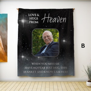 以下が含まれることがあります： 星空のデザインが施された黒いタペストリーで、「LOVE & HUGS FROM Heaven」の文字が入っています。ブレザーを着た笑顔の男性の写真も含まれています。「WHEN YOU MISS ME HAVE NO FEAR JUST HUG THIS BLANKET AND KNOW I AM HERE」の文字も表示されています。