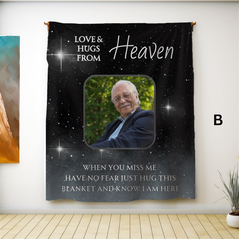 以下が含まれることがあります： 星空のデザインが施された黒いタペストリーで、「LOVE & HUGS FROM Heaven」の文字が入っています。ブレザーを着た笑顔の男性の写真も含まれています。「WHEN YOU MISS ME HAVE NO FEAR JUST HUG THIS BLANKET AND KNOW I AM HERE」の文字も表示されています。