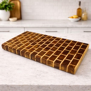 Puede incluir: Una tabla de cortar rectangular de madera con un patrón de mosaico. La tabla está hecha de bloques de madera oscuros y claros alternados, creando un diseño similar a una cuadrícula. La veta de la madera es visible y la tabla tiene una superficie lisa y acabada.