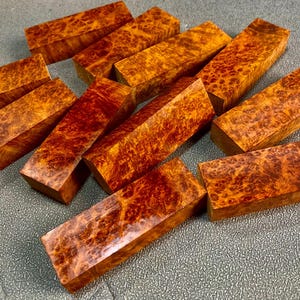 Puede incluir: Un conjunto de bloques de madera rectangulares con una paleta de colores cálidos. Los bloques muestran un patrón de veta de raíz único, con tonos marrón rojizo y amarillo dorado. Estos bloques son probablemente para proyectos de carpintería o artesanía.