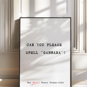 Puede incluir: Impresión tipográfica en blanco y negro con el texto "Can you please spell "Gabbana"?" y "The Devil Wears Prada - 2006" en rojo. La impresión está enmarcada en un marco negro y se muestra contra una pared blanca.
