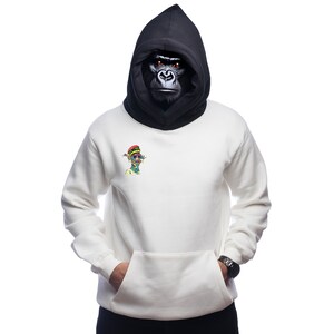May include: A white hooded sweatshirt with a black hood and a small colorful graphic on the front. The hood is pulled up and a gorilla mask is covering the face.