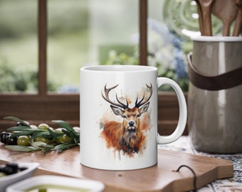 May include: White ceramic mug featuring a watercolour illustration of a red deer with antlers. The deer is looking directly at the viewer. The background is a light brown watercolour wash.