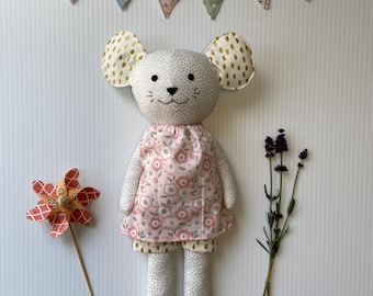 May include: A handmade mouse doll with a pink floral dress and polka dot pants. The doll has large, gold-speckled ears and a stitched face. A decorative pinwheel and lavender sprigs are next to the doll. A banner above the doll spells out "TOYLAN".