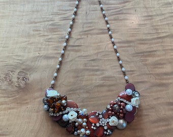 May include: A statement necklace with a cluster of red, white, and brown buttons, beads, and rhinestones. The necklace is on a white beaded chain.