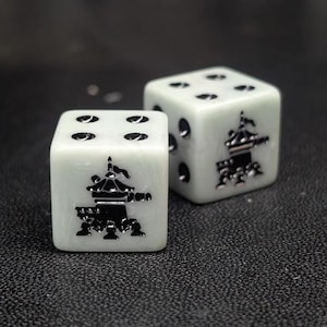 May include: Two six-sided dice with a pale, marbled off-white finish. Each die features black, recessed engravings of a traditional pagoda-style building on one face, with standard black circular pips representing the numbers on the other sides.