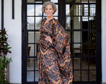 May include: A woman wearing a long, flowing, orange and black patterned dress with a V-neckline. She is standing in front of a black metal door with glass panels.