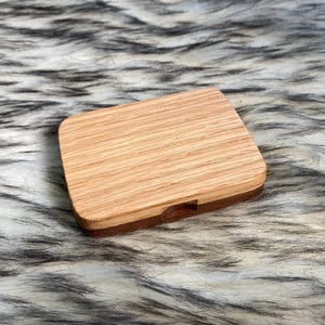 May include: A rectangular wooden box with a light brown, striped top and a darker brown base. The box is closed and sits on a fluffy, faux fur surface with black and white streaks. The wood grain is visible.