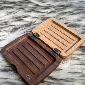 May include: An open wooden box with a hinged lid. The interior of the box is divided into sections with grooves. The box is made of two different types of wood, one light and one dark. The box is on a furry surface.