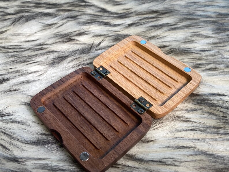 May include: An open wooden box with a hinged lid. The interior of the box is divided into sections with grooves. The box is made of two different types of wood, one light and one dark. The box is on a furry surface.