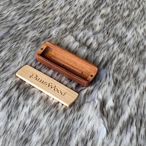 May include: A wooden box with a sliding lid, and the lid is engraved with the text "DansWood". The box is open, revealing a dark brown interior. The lid is a light tan color. The box is made of wood.