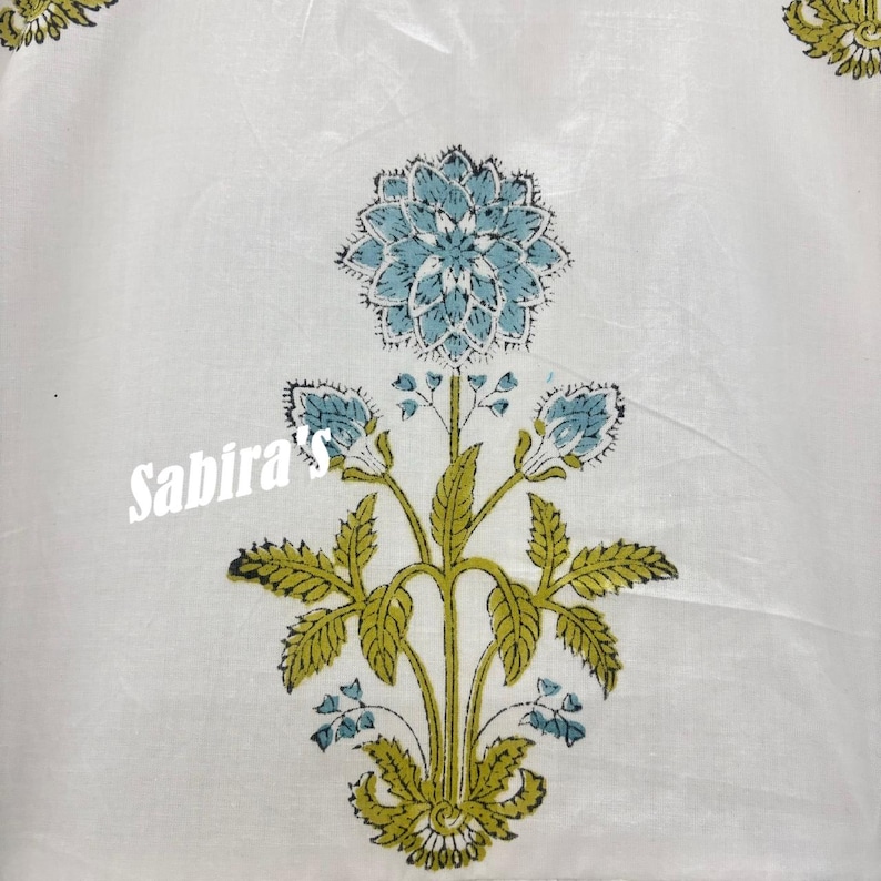 Pu&ograve; includere: Tessuto bianco con un motivo floreale blu e verde. Il design presenta un grande fiore centrale e boccioli pi&ugrave; piccoli con foglie dettagliate. Il testo "Sabira's" &egrave; stampato in bianco sull'immagine.